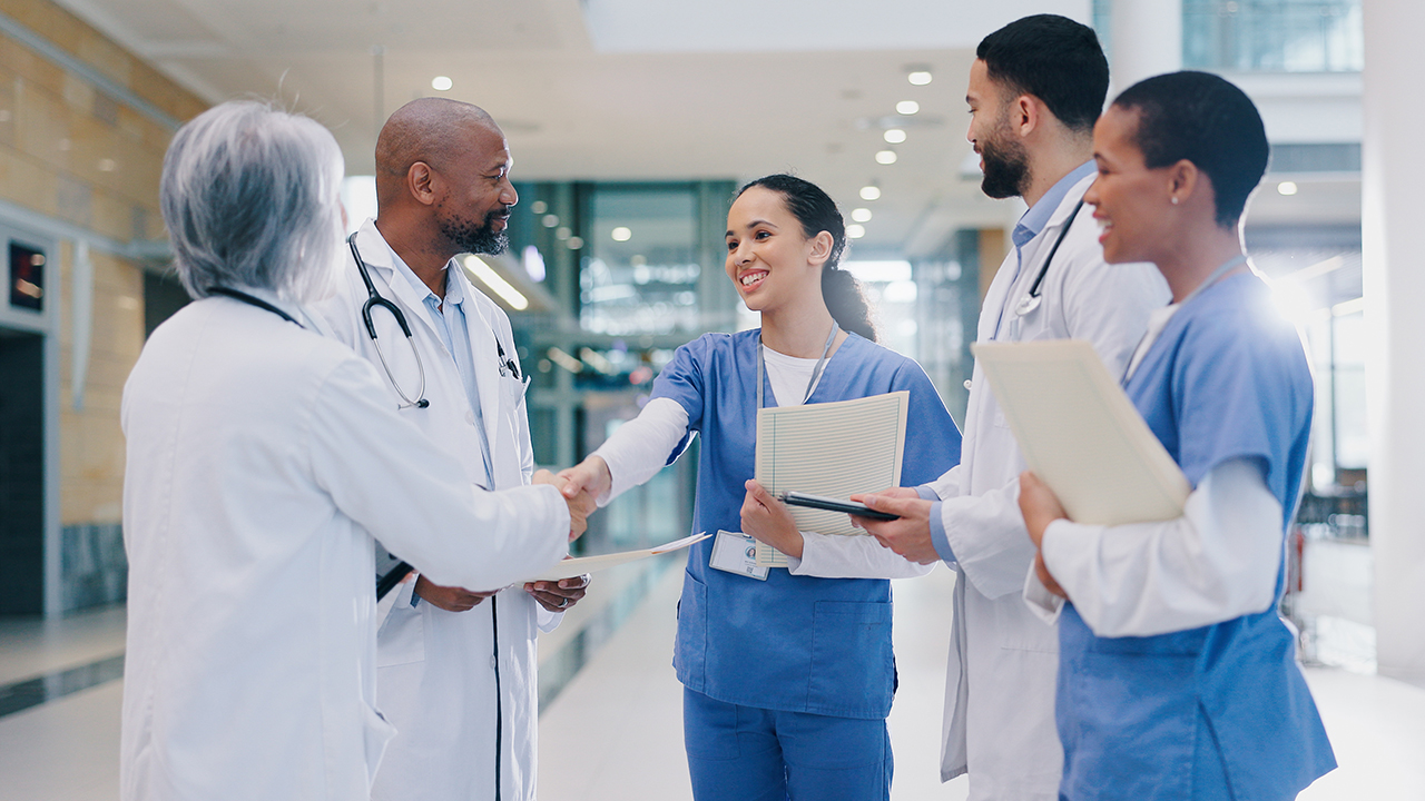 A team of doctors and nurses in a  hospital corridor shaking hands and introducing a new employee