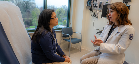 A woman converses with a doctor in a hospital room, discussing her health and treatment options.