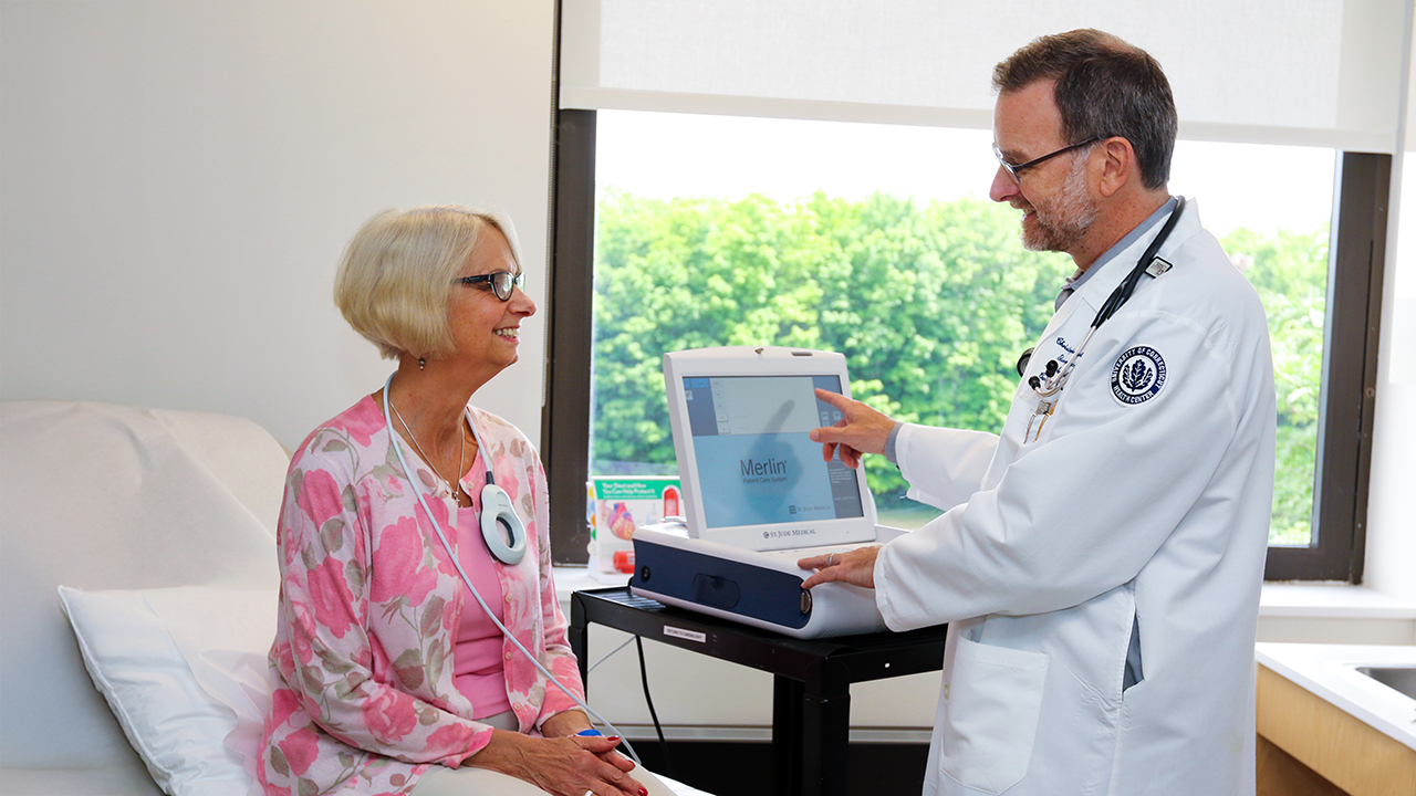 Dr. Christopher Pickett, pointing to a monitor screen, explaining test results to a patient