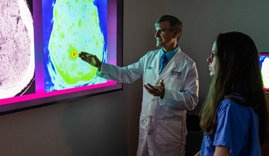 A doctor and a patient examining a medical screen together in a clinical setting.