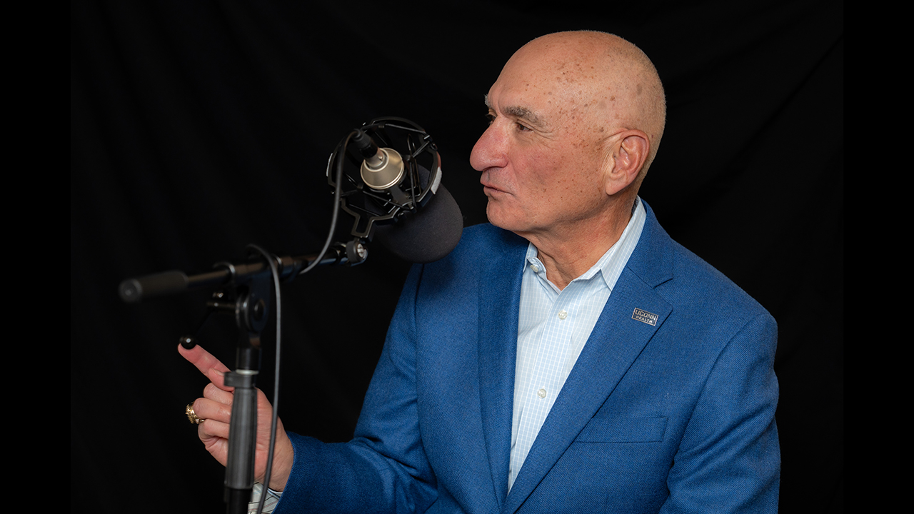 Dr. Anthony Alessi speaking into a microphone and pointing a finger